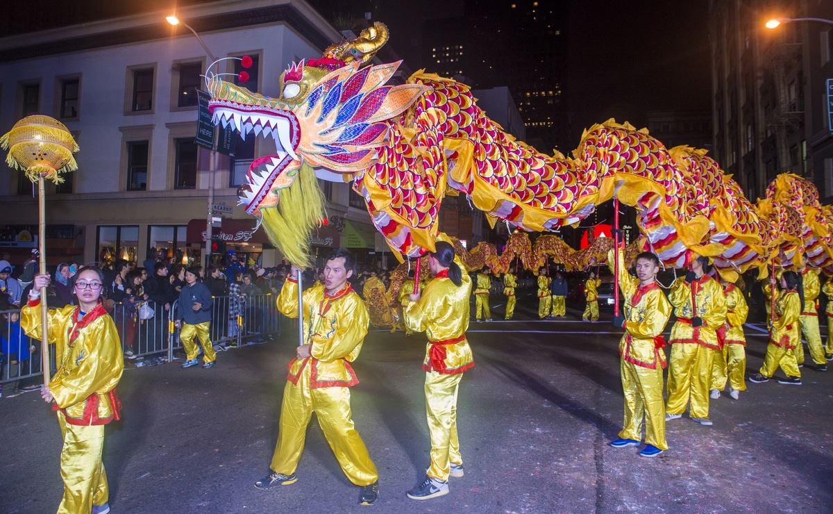 A group of people dressed in yellow hoists a large yellow and red dragon parade float over their heads.