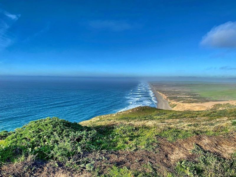 View of Drakes Beach at Point Reyes with raw coastline and bright blue water.