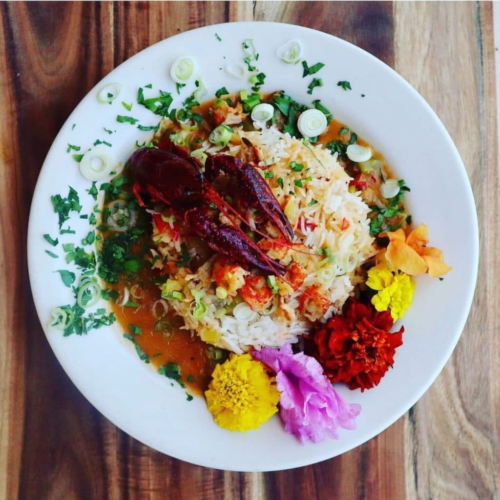 A colorful dish from Voodoo Love restaurant, with a crawfish on a bed of rice with green onions and flowers.