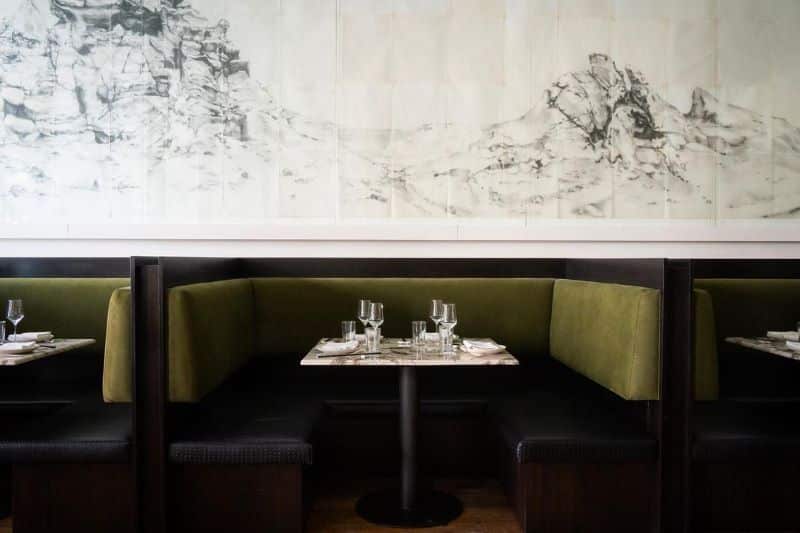 An empty dining table with green sofa seating and a black and white art piece on the wall.