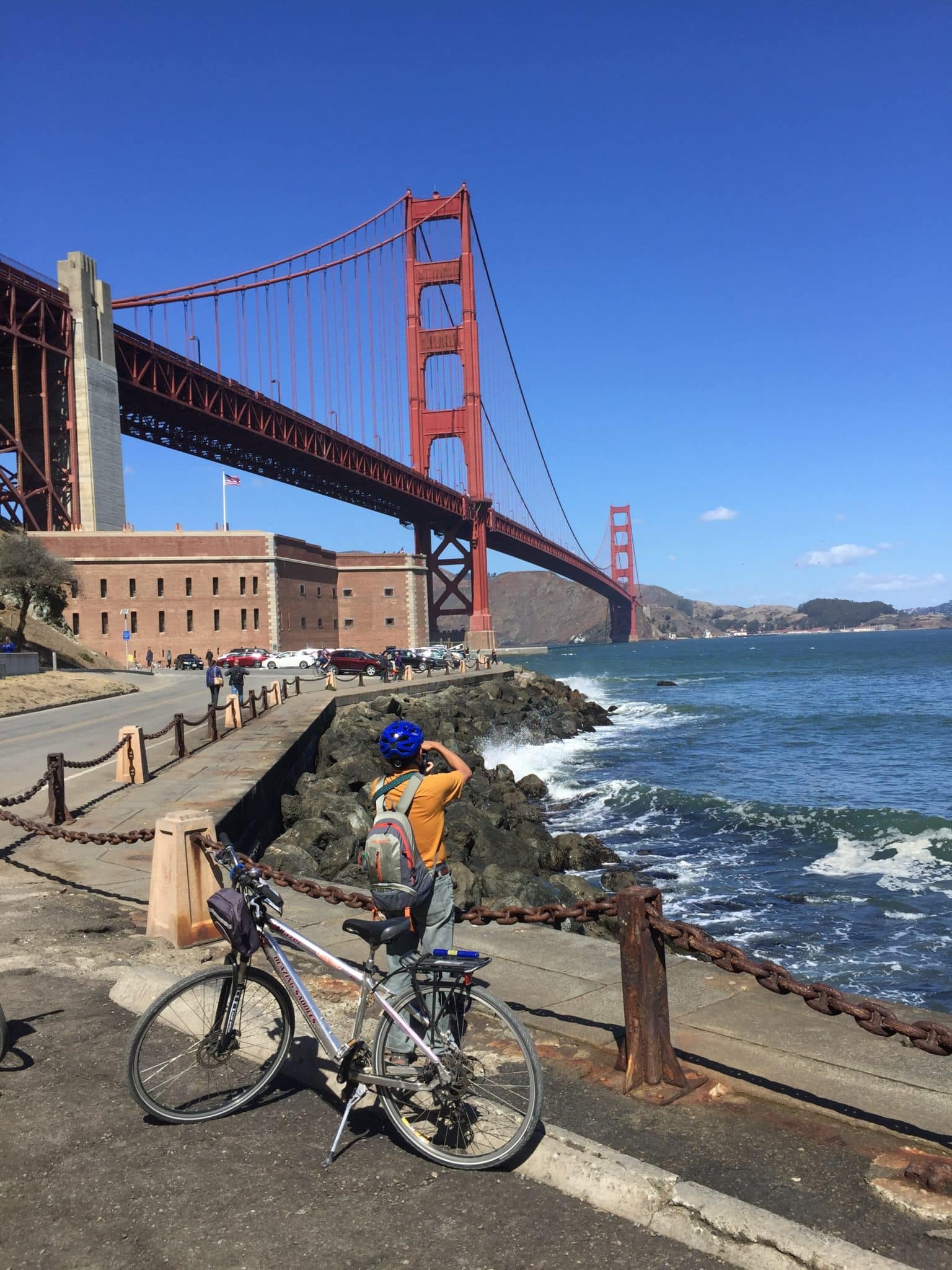 A man with a bike takes a photo of the Golden Gate Bridge