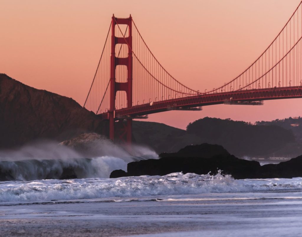 Golden Gate Bridge at sunset with a foreground of waves crashing on the beach.