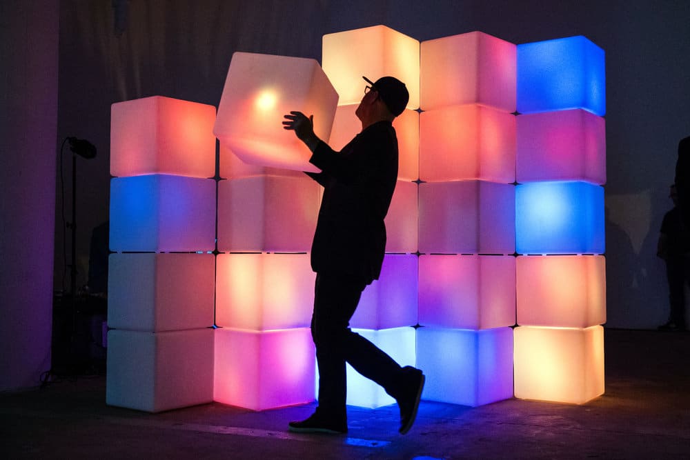 A man interacts with a sculptural stack of glowing cubes