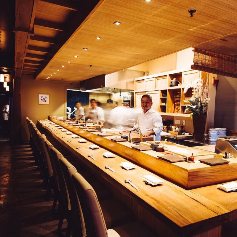Sushi chefs work behind the counter at a long bar set for service.