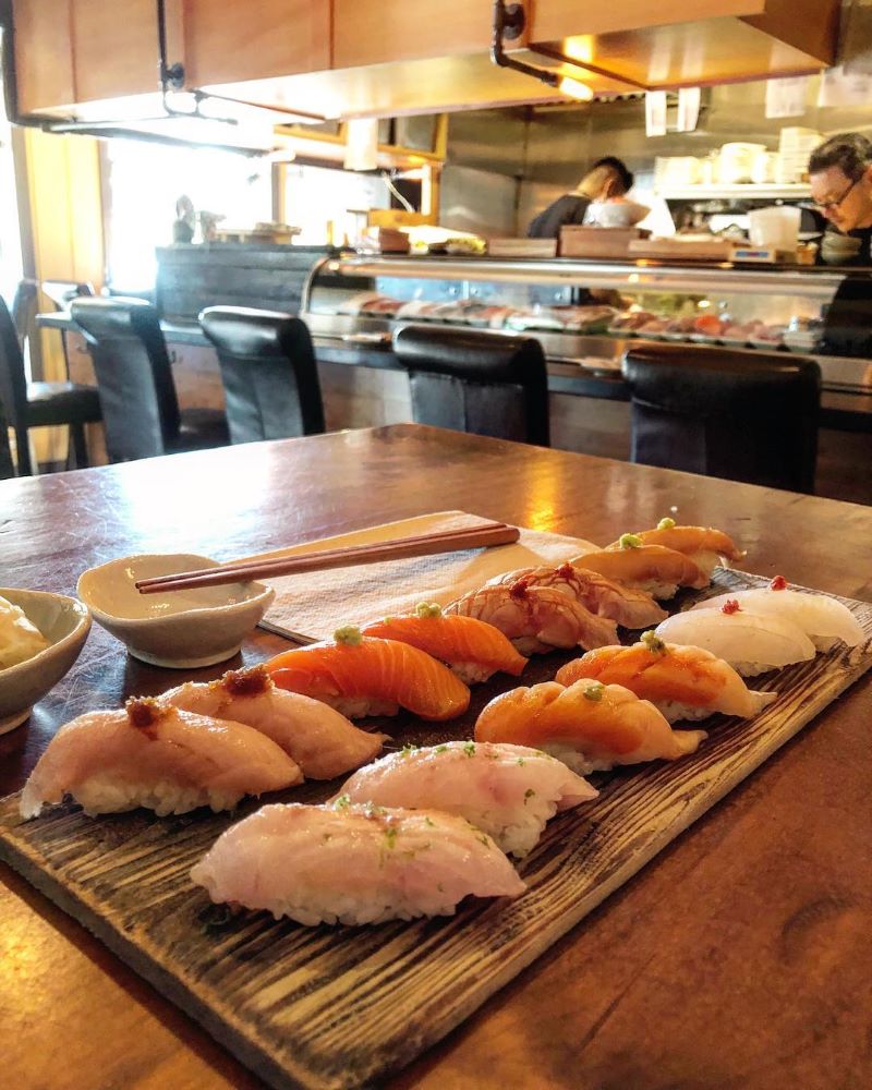 A plate of nigiri on a table in the foreground with sushi kitchen and bar seating in the background.