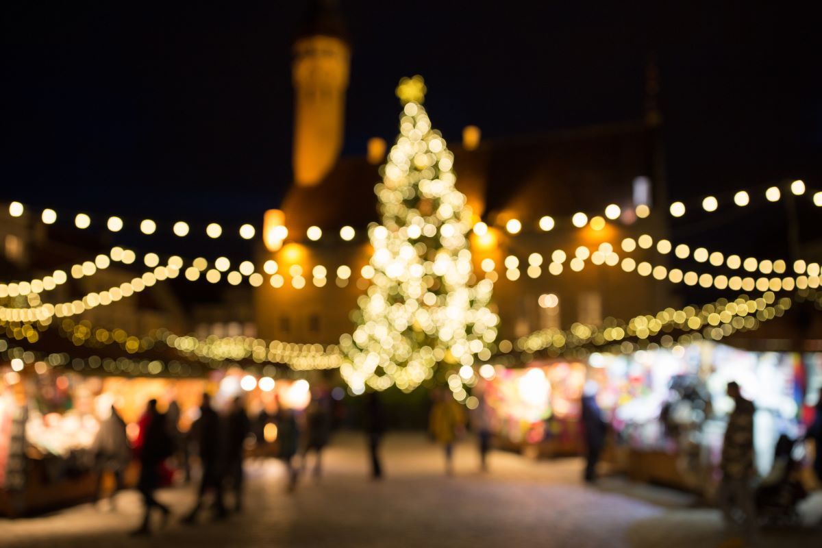 An out-of-focus glowing holiday market with string lights and a tree.