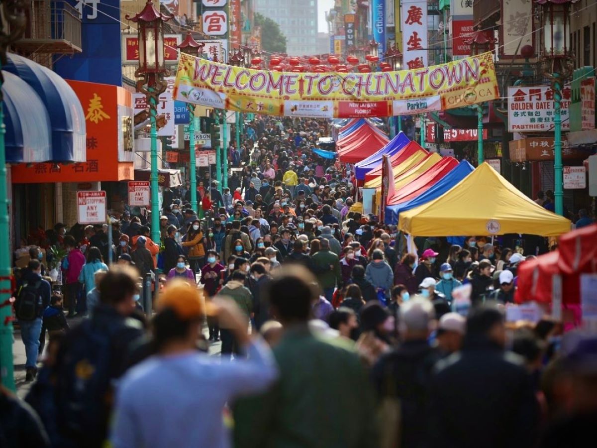A massive crowd of people takes up a colorful street with a banner over it that reads "Welcome to Chinatown"