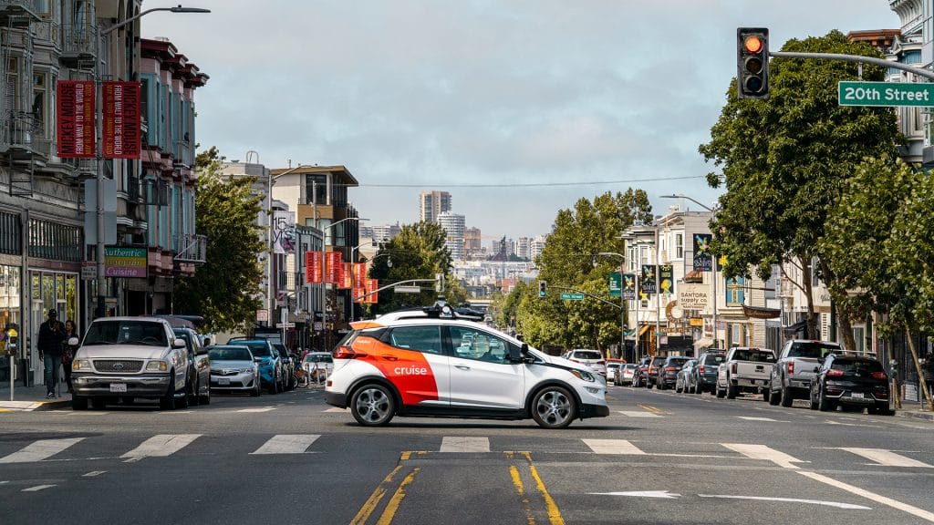 A white and orange driverless Cruise car crossing an intersection in San Francisco.