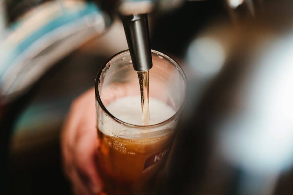 A bartender fills a beer glass from a tap.