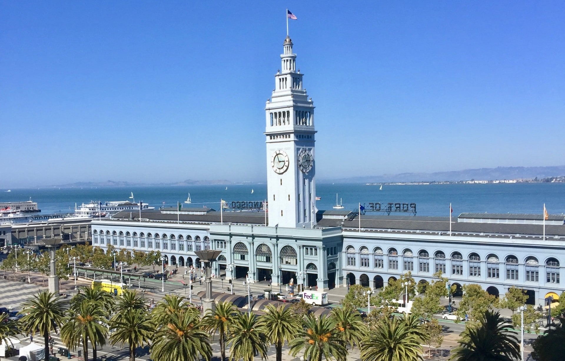 San Francisco's Ferry Building with a line of palm trees in front and Bay views in the background.
