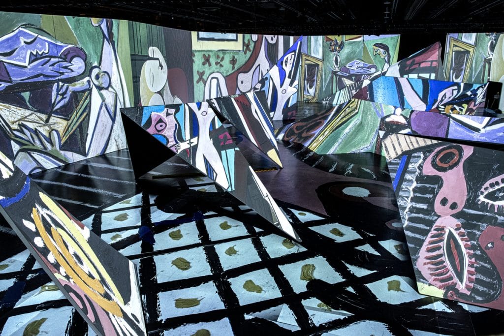Imagine Picasso: The Immersive Exhibition showcasing Picasso's colorful creations projected on a dynamic indoor space with triangular sculptures.