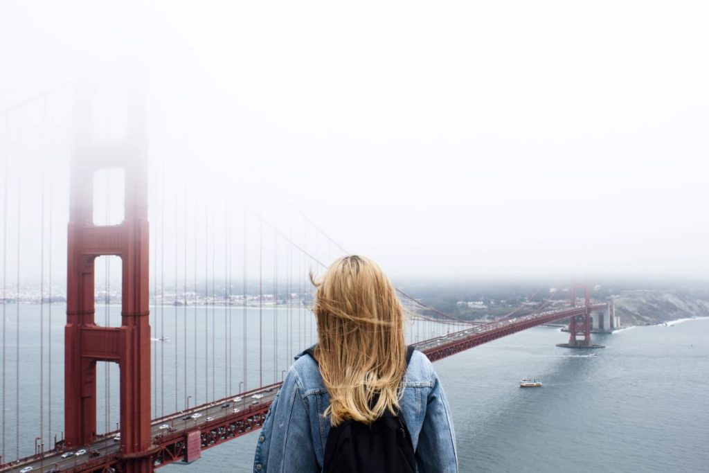 A blonde woman watches the Golden Gate Bridge on a foggy day.