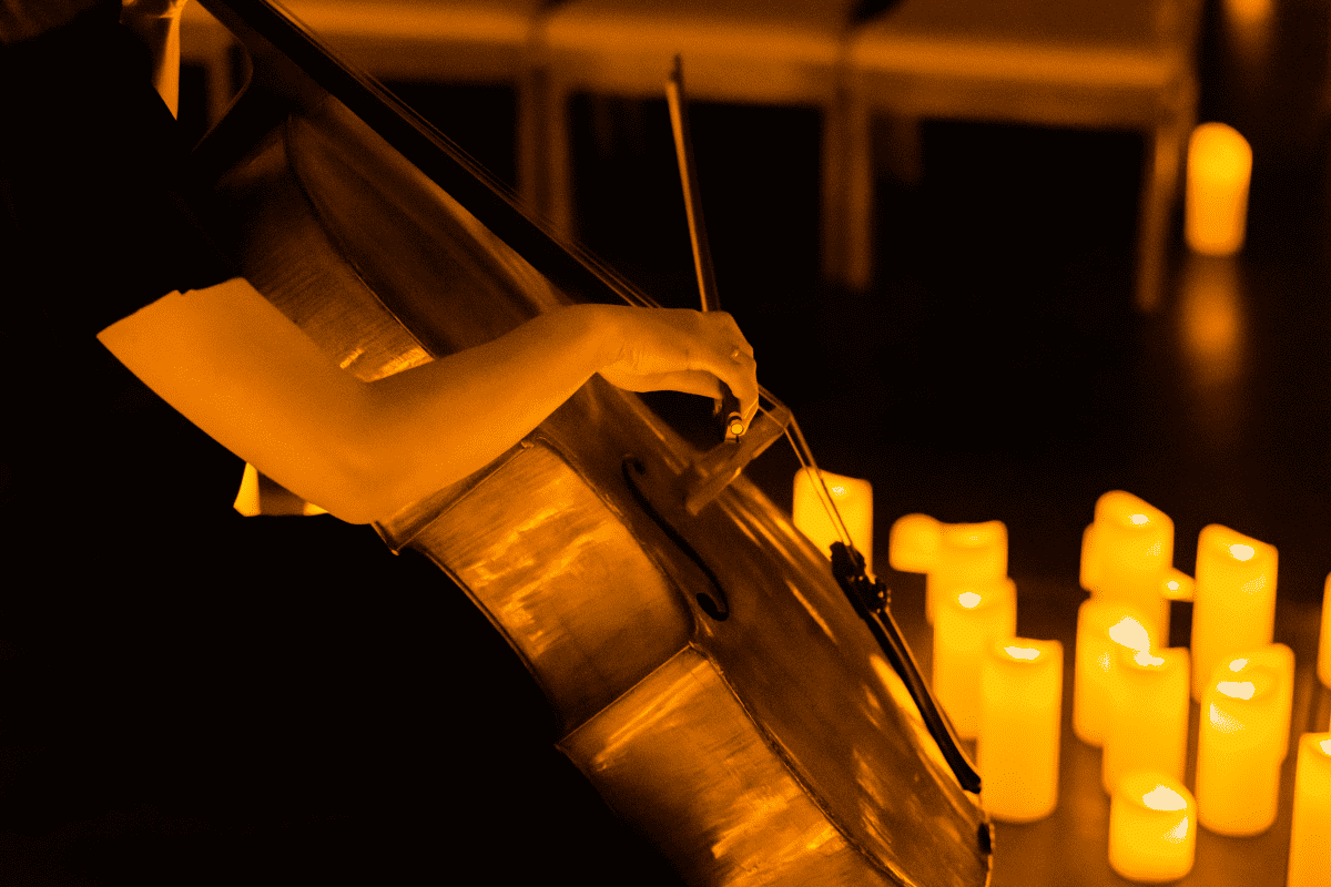 A close up of a woman playing the cello with some candles on the ground beside her.