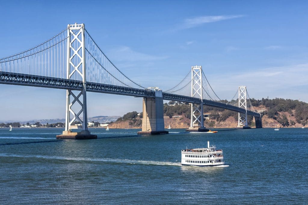 A San Francisco Ferry passes alongside the Bay Bridge.