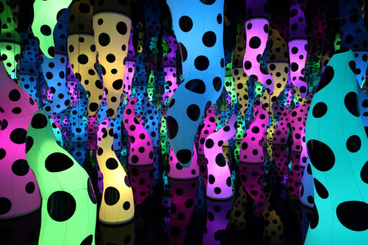 A darkened mirror room with luminous polka-dot tentacles stretching from floor and ceiling.