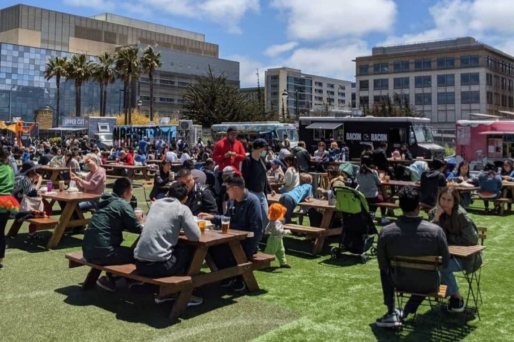 Crowds of people eat and drink at picnic tables at Spark Social SF on a sunny day.