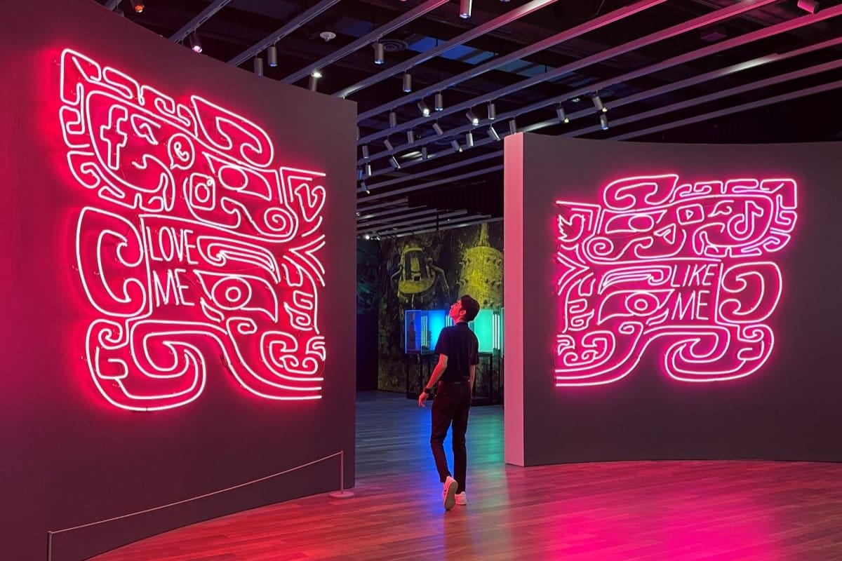 A man walks between two pink glowing neon art pieces with various social media icons hidden in them.