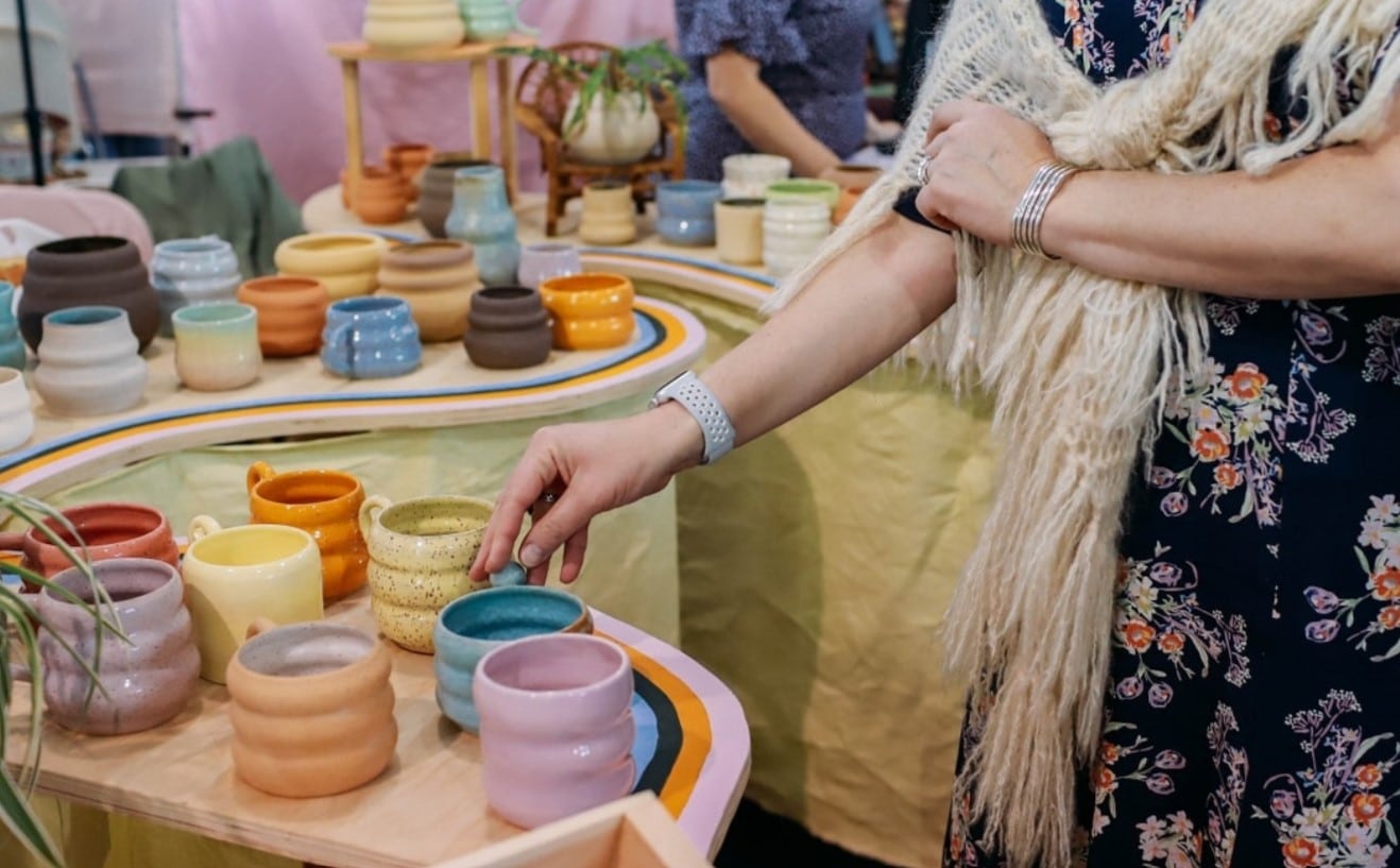 A woman touches colorful handmade mugs.