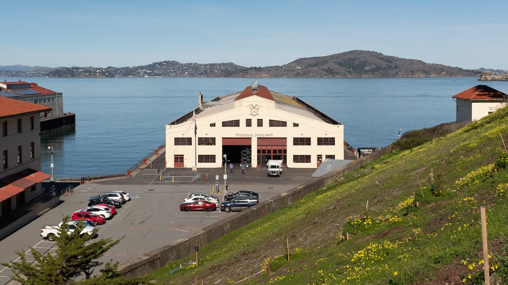 Fort Mason Center pavilion from above, with the Bay in the background and a grassy hill in the foreground.
