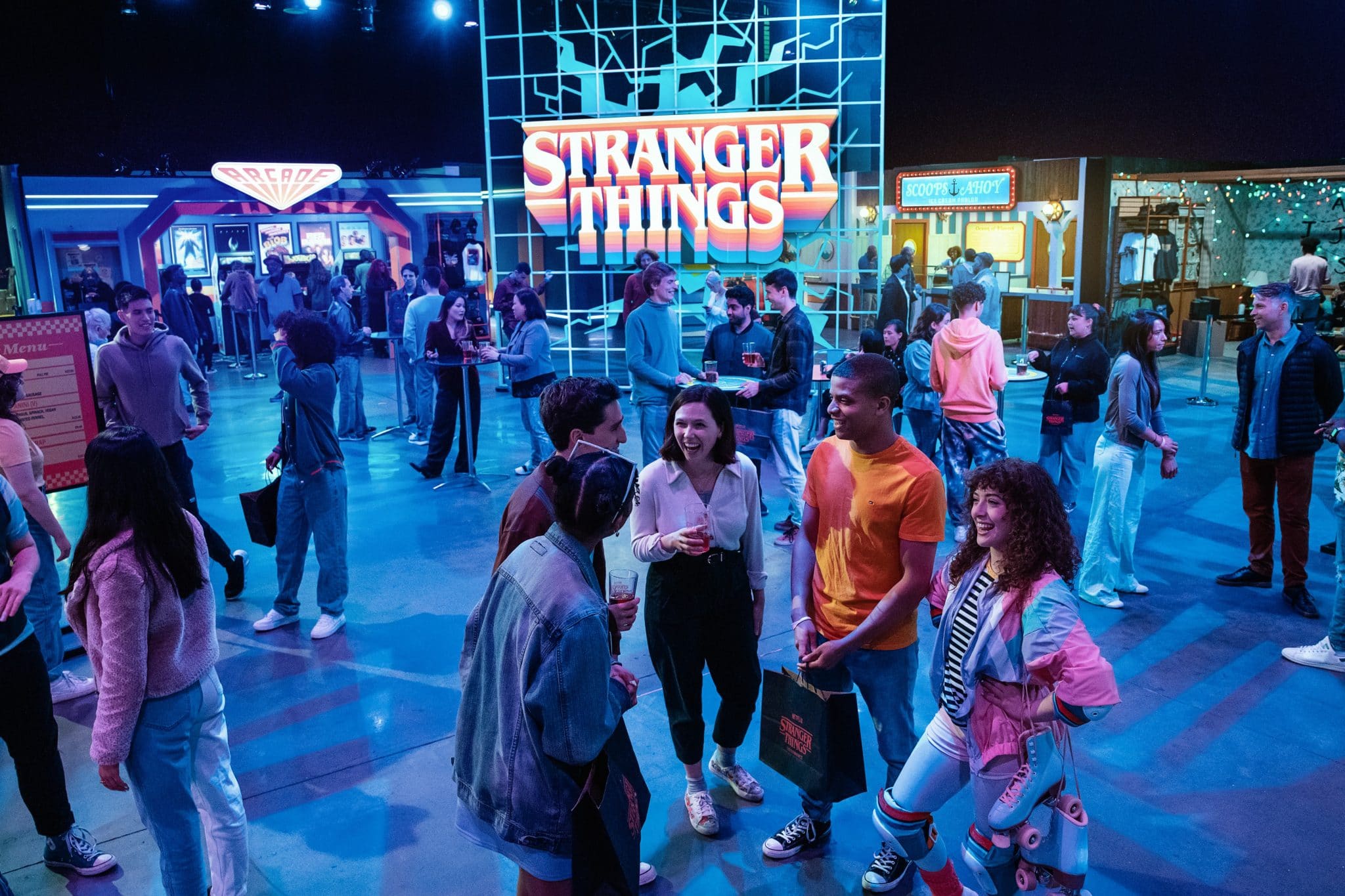 Stranger Things Experience's Mix-Tape area, with a large glowing Stranger Things logo and people walking around, chatting, and enjoying cocktails.