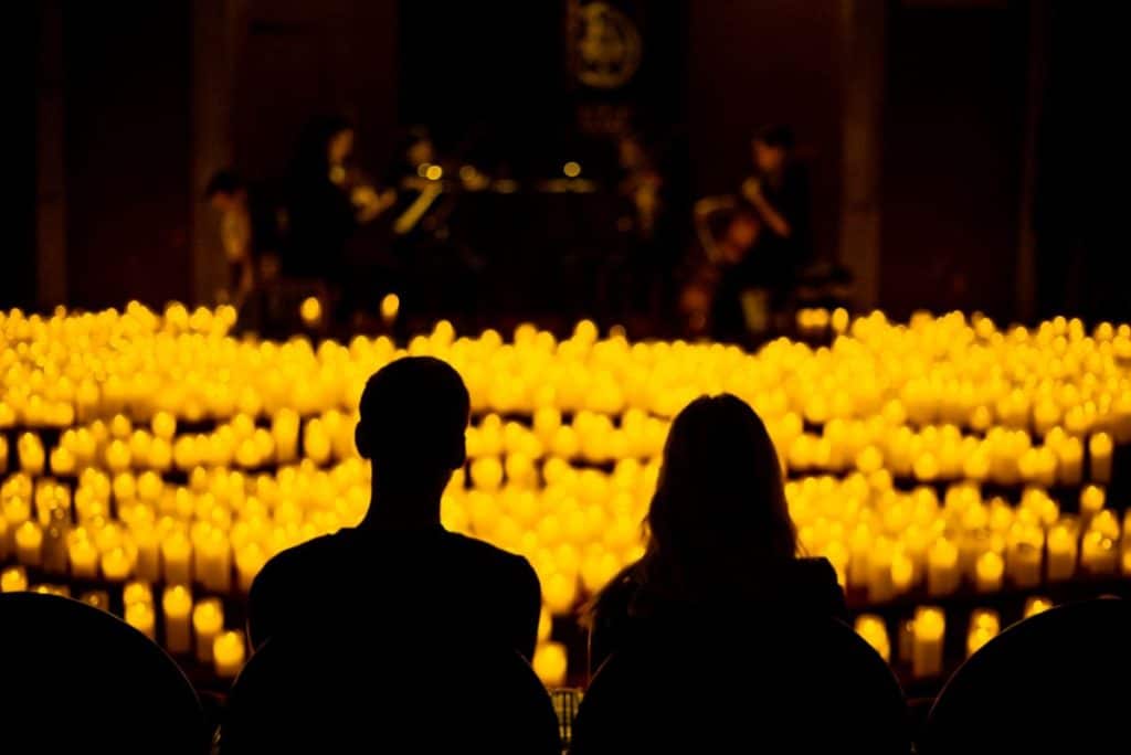 Two silhouetted people watch a candlelight concert.