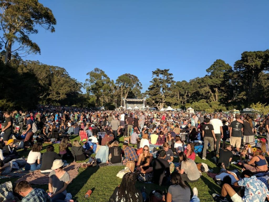 A crowd of people sits on the grass in front of a stage in the distance at Hardly Strictly Bluegrass.