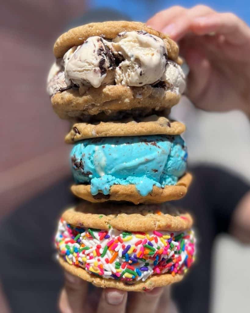 A person holds a stack of 3 ice cream cookie sandwiches in various flavors.