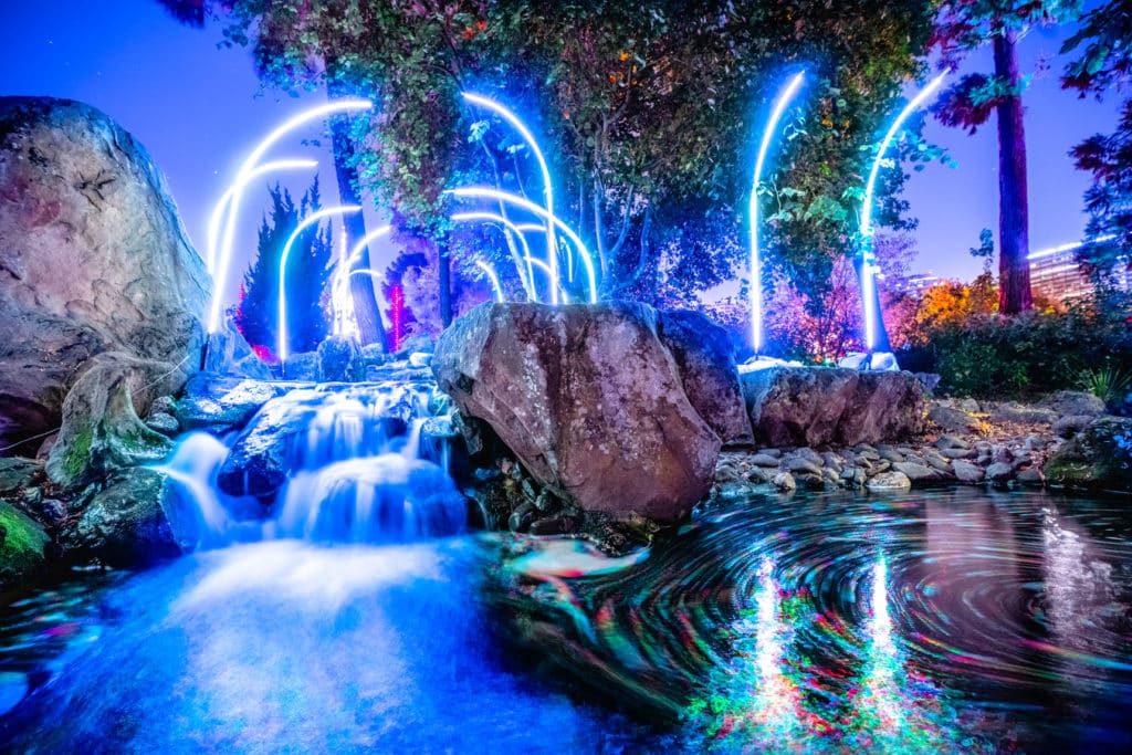 A series of glowing blue arches over a garden with a small waterfall.