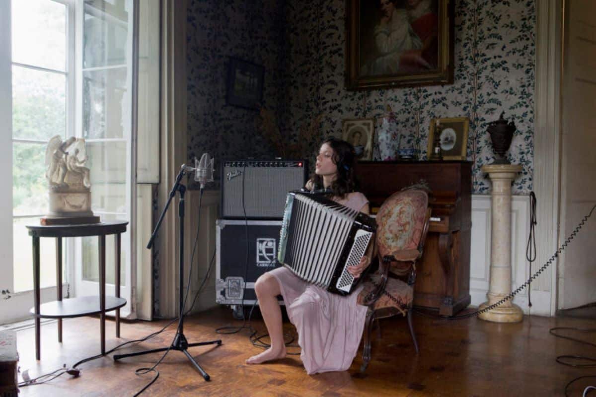 A woman plays an accordion and sings in a video still from 'The Visitors'