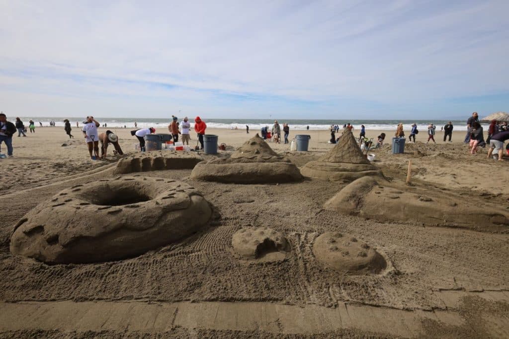 People walk around giant sandcastles at the Leap Sandcastle Classic competition at Ocean Beach