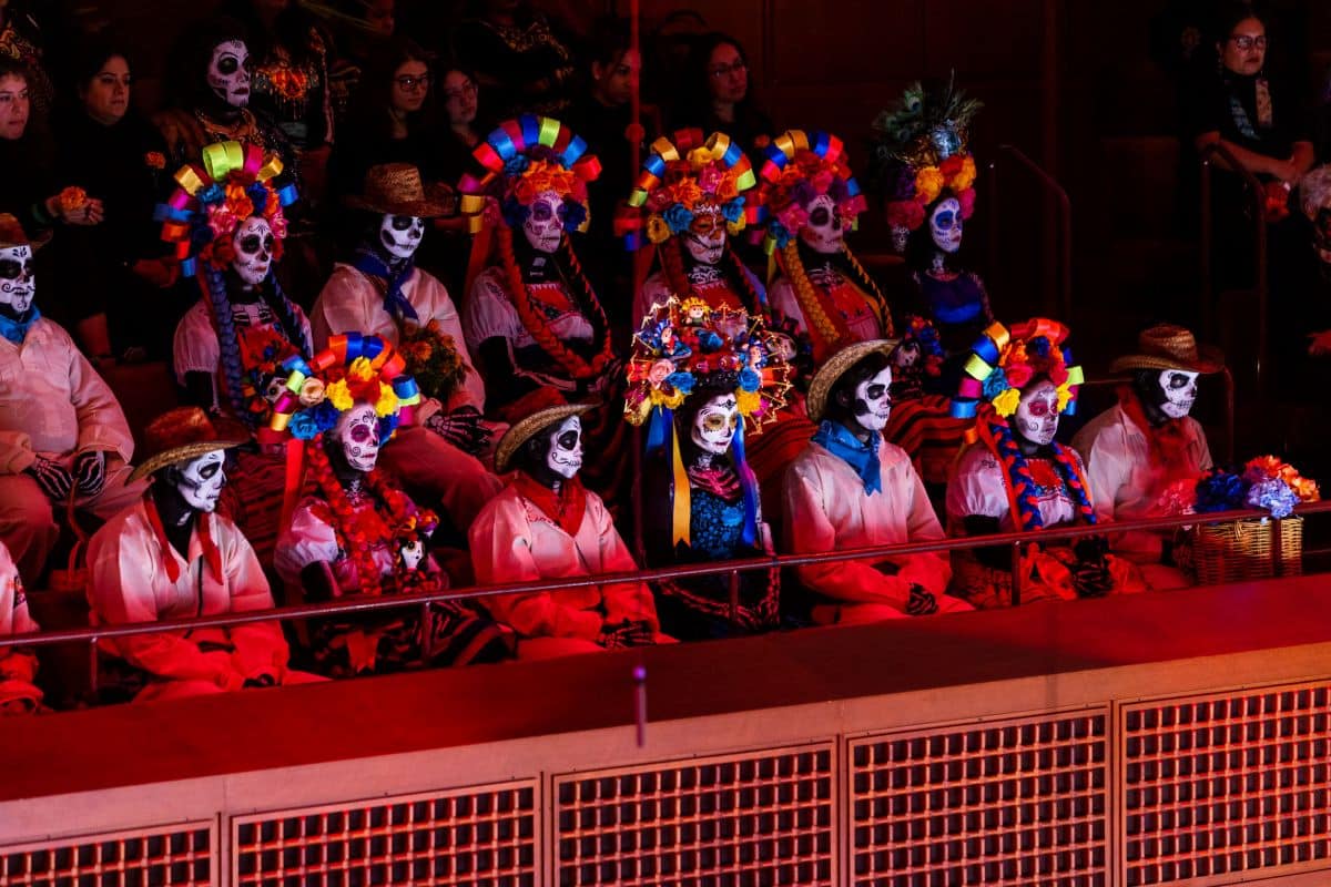 A group of seated people dressed in colorful Día de los Muertos attire.