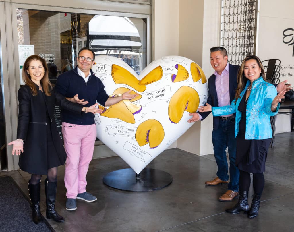 A group of people poses next to a large white heart sculpture decorated with pictures of fortune cookies.