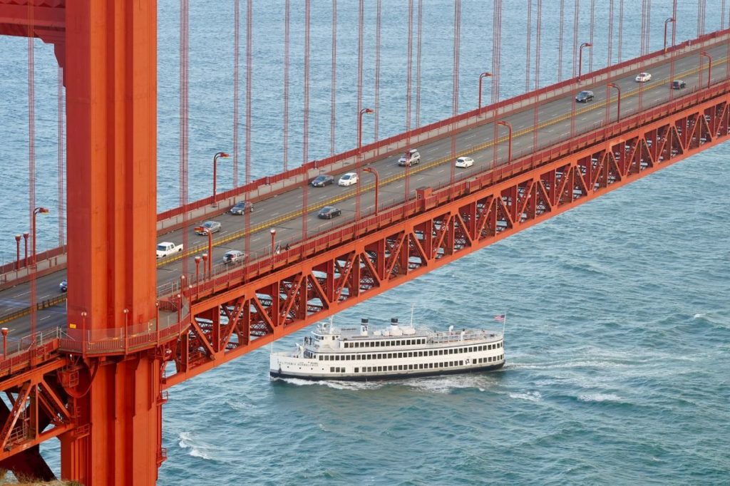 A white ferry boat crosses under the Golden Gate Bridge.