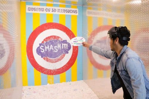 A man throws a plate a a wall reading "Smash It"
