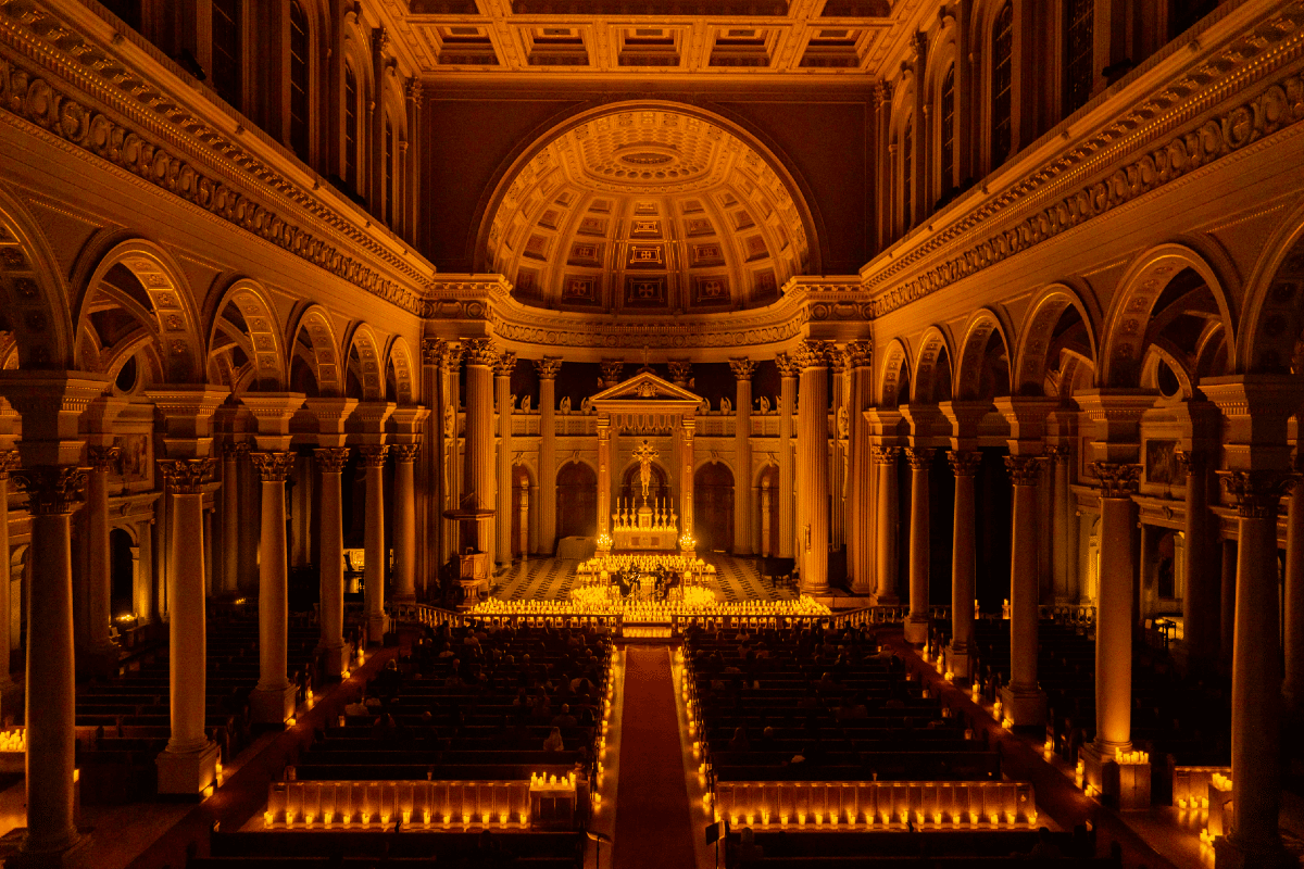 interior of a church, displaying the entire nave lit up in a golden glow of hundreds of candles one of the Candlelight concerts in San Francisco.