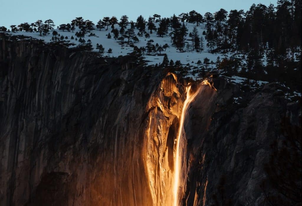 A bright gold, glowing stream of water runs down a snowy cliffside.
