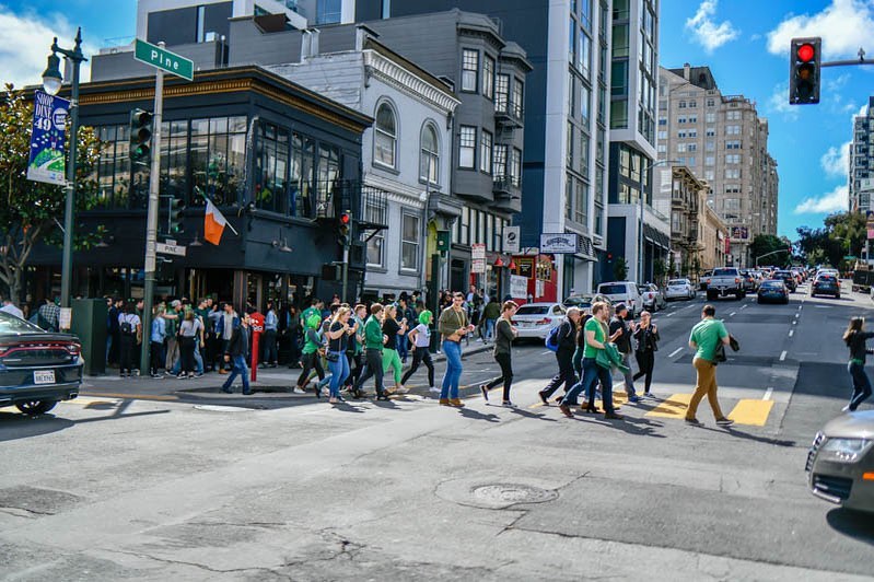 A crowd of people dressed in green crosses a street at the St Patrick's Day pub crawl.