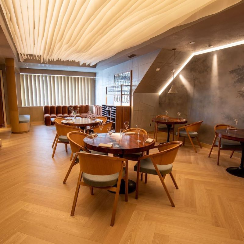 An empty dining room with warm-toned wooden floors and chairs and soft ambient lighting.