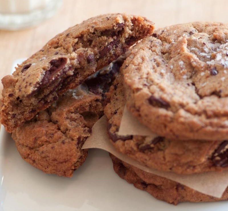 A stack of gooey chocolate chip cookies with a few broken in half.