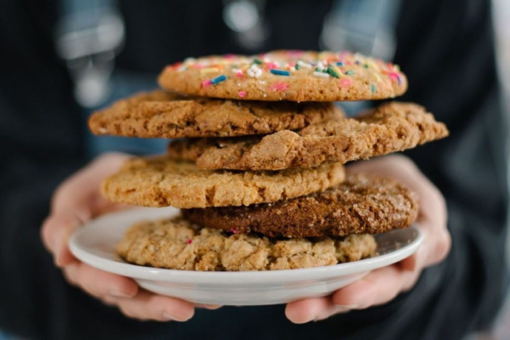 A person holds a stack of various cookies on a plate.