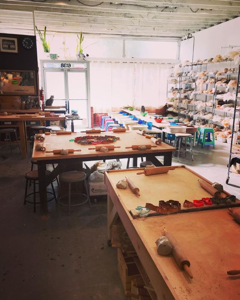 A pottery studio with big wooden tables set up with rolling pins, cookie cutters, and hand building tools.