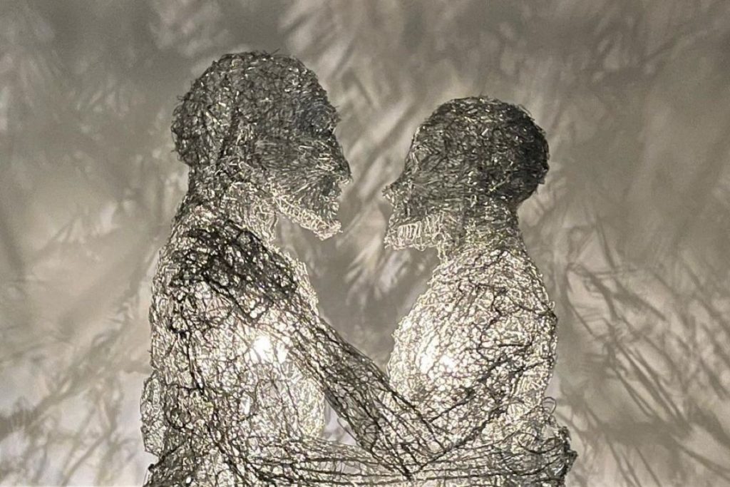 A lighted sculpture of human figures embracing made out of paperclips.