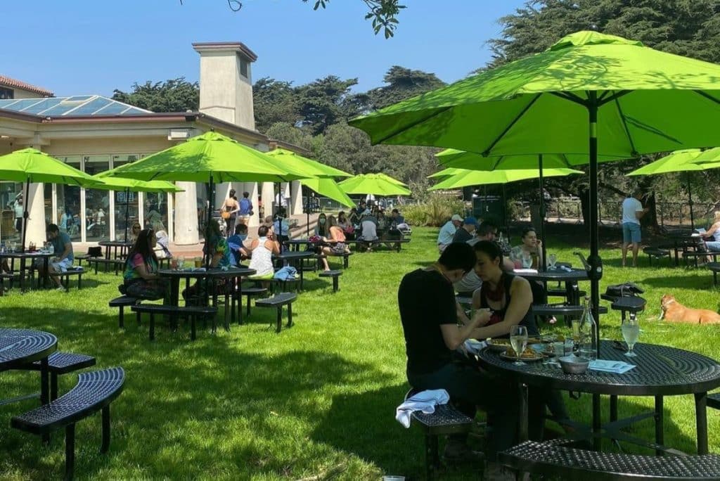 People sit at outdoor tables under green umbrellas.