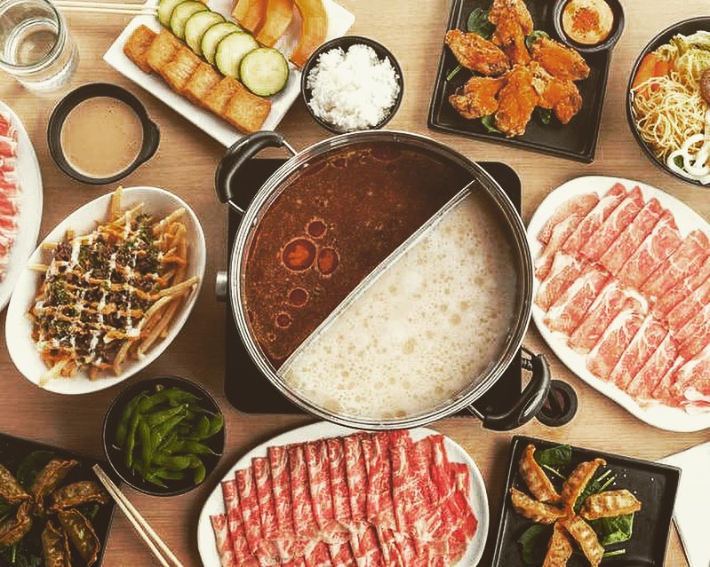 A shabu-shabu setup with a boiling pot of soup in the middle surrounded by sides including meats and vegetables.