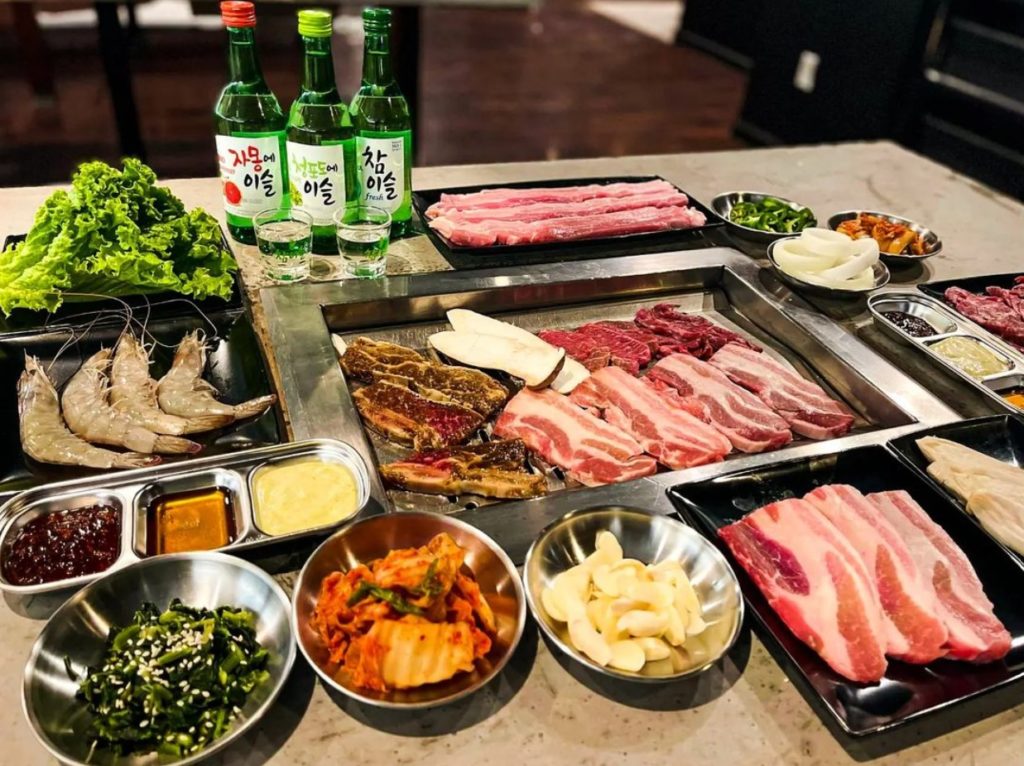 A grill-your-own Korean barbecue spread with assorted meats, veggies, sides, and shots of sake.