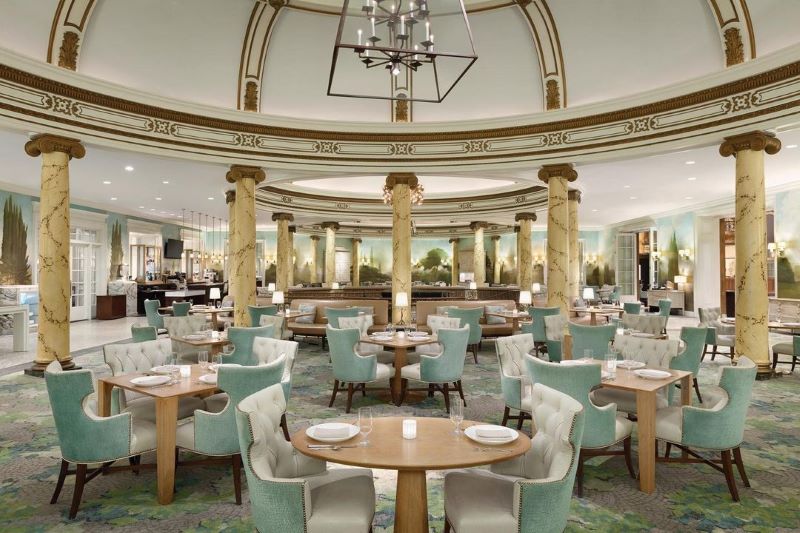 Fairmont Hotel's dining room with light blue plush chairs around wooden tables and golden marble columns in the background.