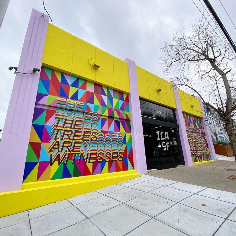 Exterior of ICASF building painted in yellow and purple with a geometric colorful mural reading "The trees are witnesses." 