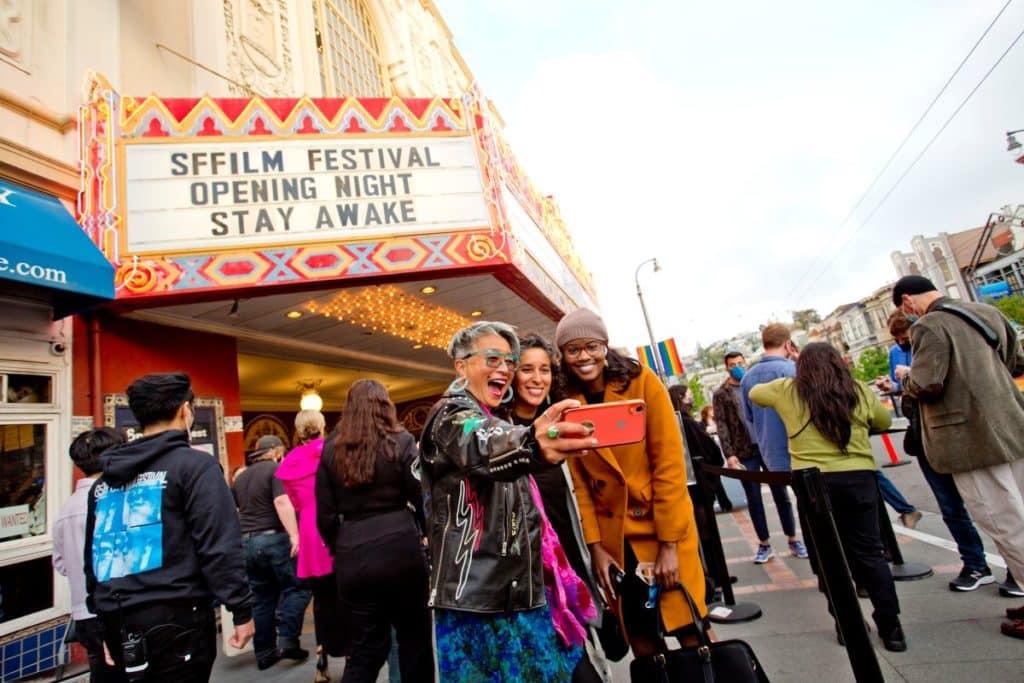 Three people take a selfie in front of the Castro Theatre's marquee.