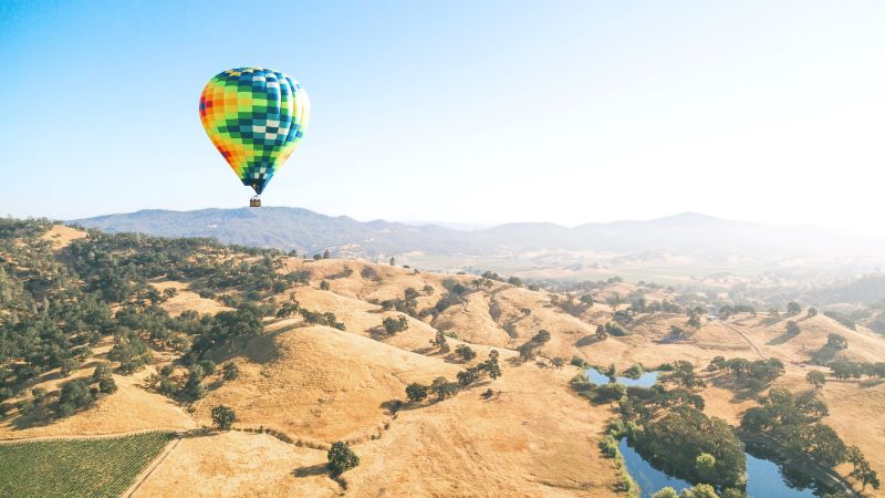 A rainbow hot air balloon floats over the countryside in Napa Valley.