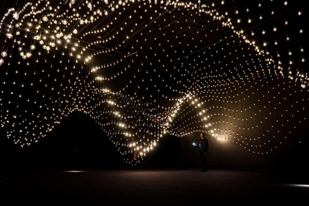 A person stands beneath thousands of suspended lightbulbs.